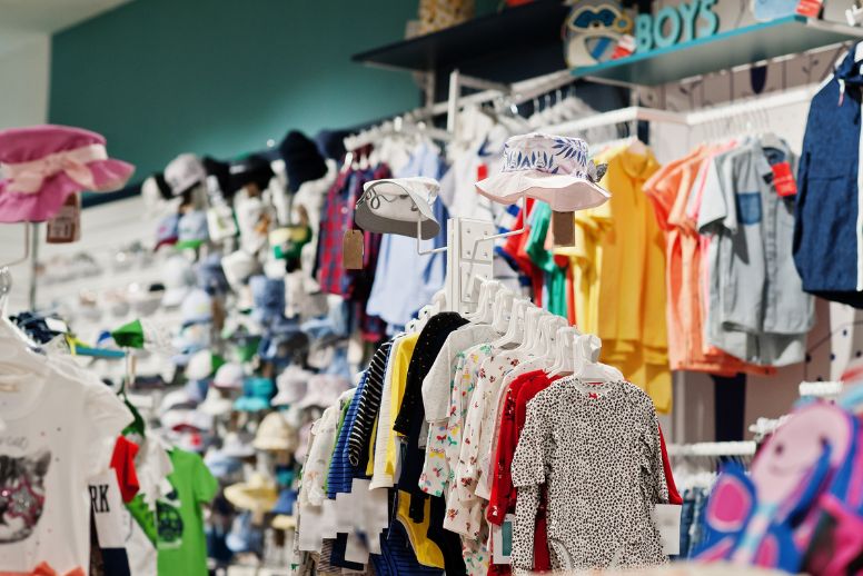 A imagem mostra uma loja de roupas de criança com várias peças penduradas.