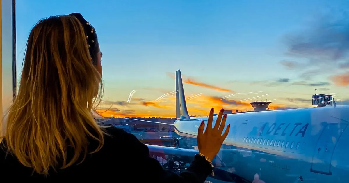 Fernanda Batista (Orlando Diferente) olhando para avião no aeroporto durante pôr do sol