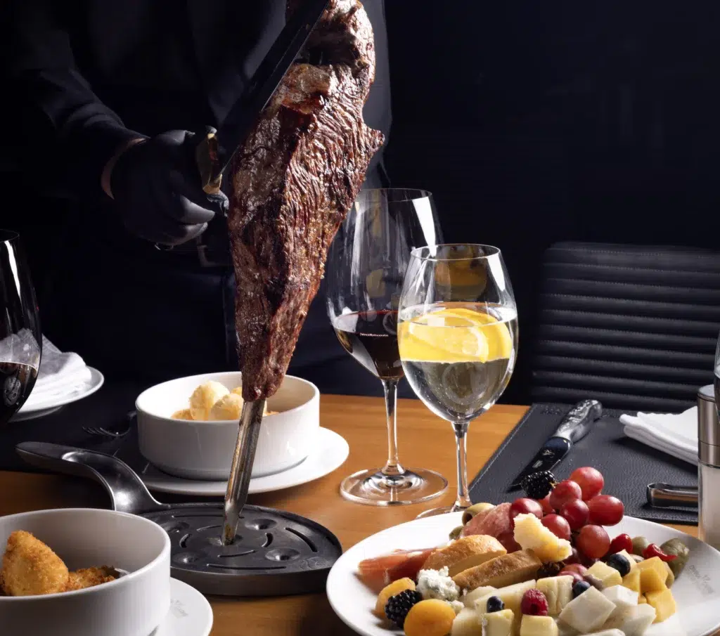 Foto do restaurante Divina Carne em que mostra opções do buffet, vinhos e a carne sendo servida