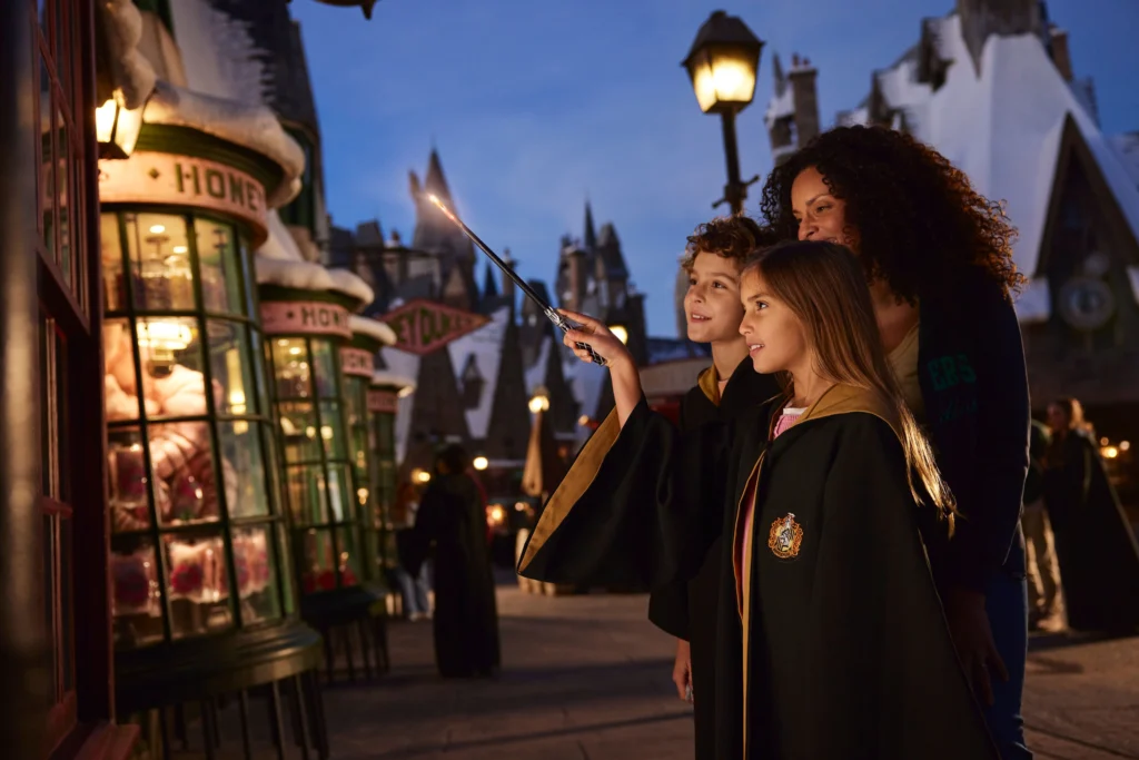 Família com adulto e crianças, vestidas com uniformes de Hogwarts e com varinhas no parque Universal